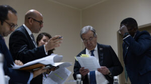 UN chief Antonio Guterres reads a negotiating text surrounded by advisers at Cop28 climate talks